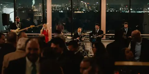 A live band performing at an event with a city skyline visible in the background.