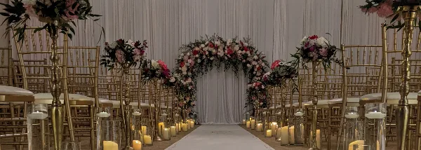 Elegant wedding ceremony aisle with white chairs, floral arch, and warm candlelight