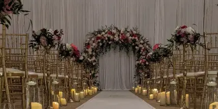 Elegant wedding ceremony aisle with white chairs, floral arch, and warm candlelight