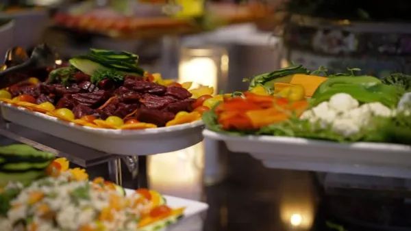 A catering buffet featuring a platter of sliced roasted meat and a side of fresh vegetables and cheese.