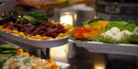 A catering buffet featuring a platter of sliced roasted meat and a side of fresh vegetables and cheese.