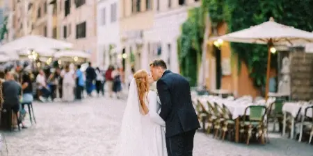 A bride and groom kissing on a cobblestone street with outdoor cafe seating in the background.