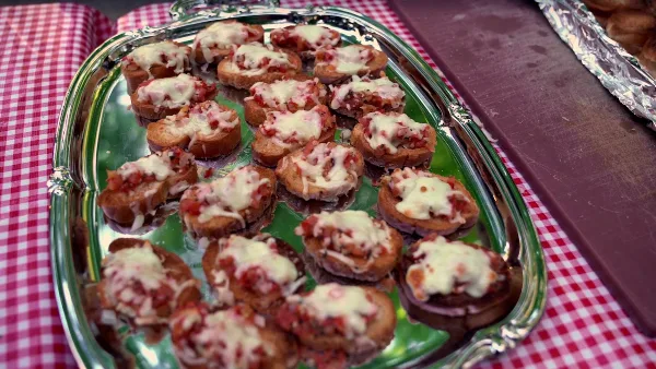 A silver platter of bruschetta appetizers served on a red and white checkered tablecloth.