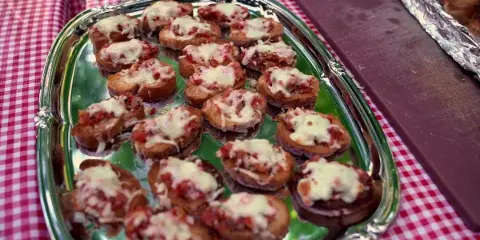 A silver platter of bruschetta appetizers served on a red and white checkered tablecloth.