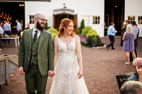 A bride and groom holding hands and walking outdoors at a wedding reception.