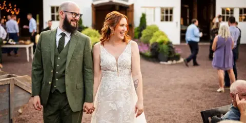 A bride and groom holding hands and walking outdoors at a wedding reception.
