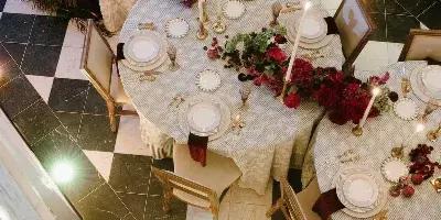 Overhead view of an elegant wedding reception table setting featuring white linens, red floral arrangements, and tall candles on a checkered floor.