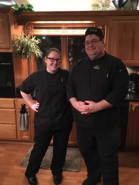 Two chefs in black uniforms standing in a kitchen setting
