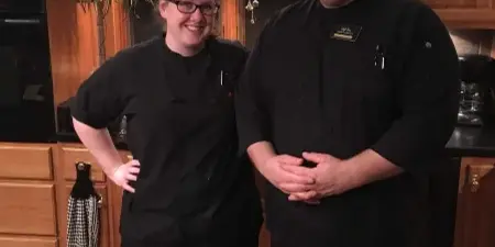 Two chefs in black uniforms standing in a kitchen setting
