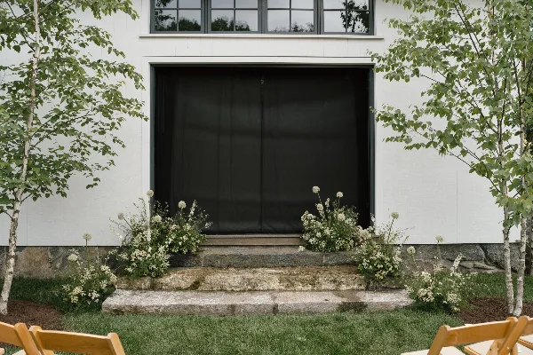 Floral arrangements decorating the stone steps and entrance of a white wedding venue building.