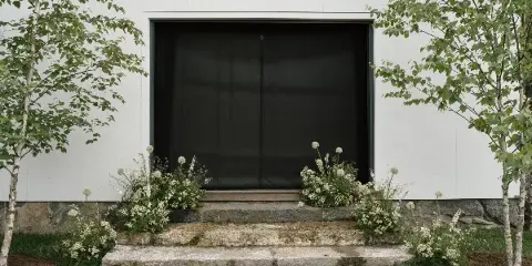 Floral arrangements decorating the stone steps and entrance of a white wedding venue building.