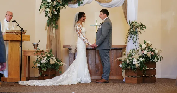 Bride and groom holding hands at the altar during a wedding ceremony in a white chapel.