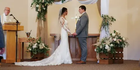 Bride and groom holding hands at the altar during a wedding ceremony in a white chapel.