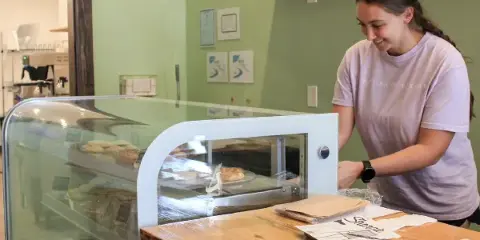 Bakery staff member in a branded shirt serving customers at a glass display case filled with baked goods.