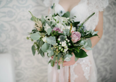 A bride holding a lush wedding bouquet with white and pink flowers and greenery.