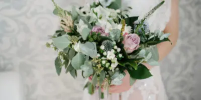 A bride holding a lush wedding bouquet with white and pink flowers and greenery.