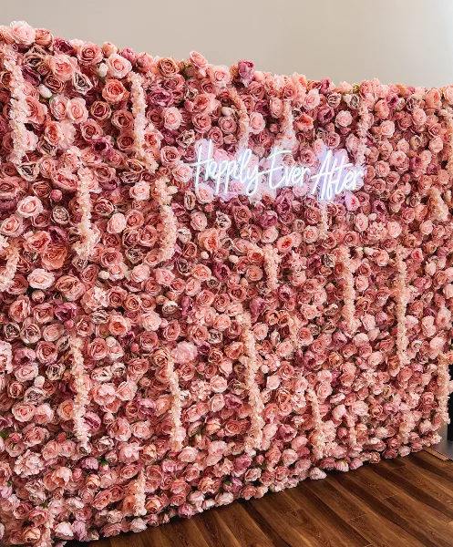 A large pink floral wall backdrop featuring a 'Happily Ever After' neon sign.