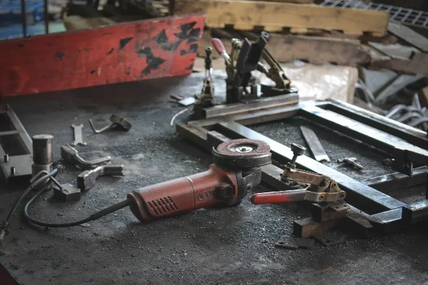 A red angle grinder and metalworking tools resting on a dusty workbench.