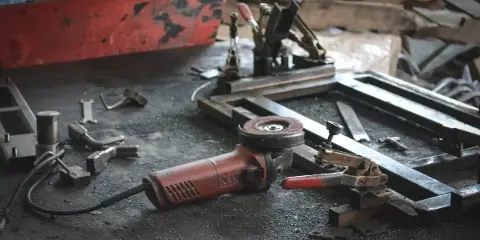 A red angle grinder and metalworking tools resting on a dusty workbench.