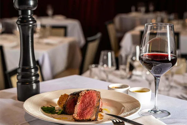A plated steak dish with a glass of red wine on a restaurant table setting.