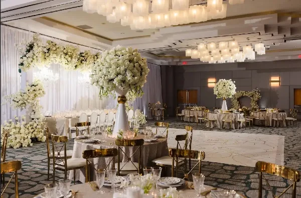 Luxury event venue interior featuring white floral arches, large floral centerpieces, and gold Chiavari chairs.