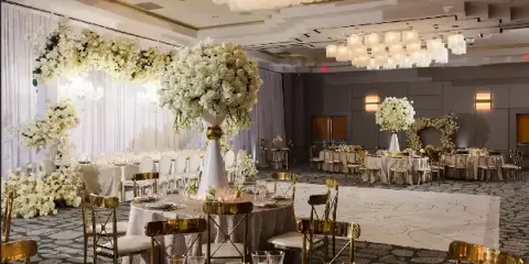Luxury event venue interior featuring white floral arches, large floral centerpieces, and gold Chiavari chairs.