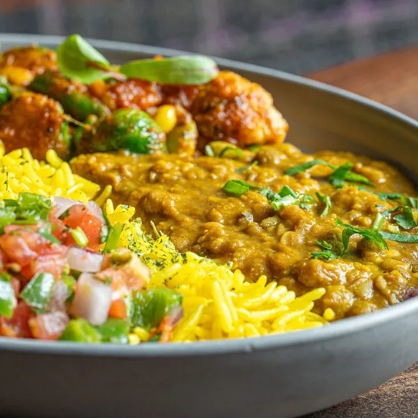 A close-up of a Curry Up Now bowl featuring lentil curry, yellow rice, and roasted vegetables.