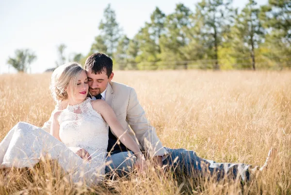 A bride and groom sitting together in a field of tall golden grass.
