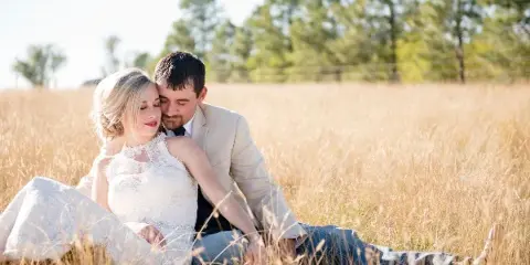 A bride and groom sitting together in a field of tall golden grass.