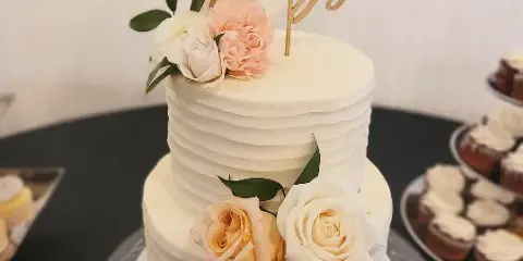 A two-tier white wedding cake with fresh floral decorations and a gold 'The Kings' topper.