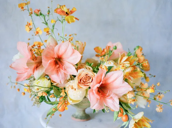 A floral arrangement featuring pink lilies, peach roses, and yellow orchids in a decorative vase.
