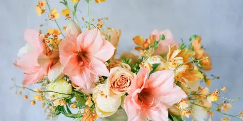 A floral arrangement featuring pink lilies, peach roses, and yellow orchids in a decorative vase.