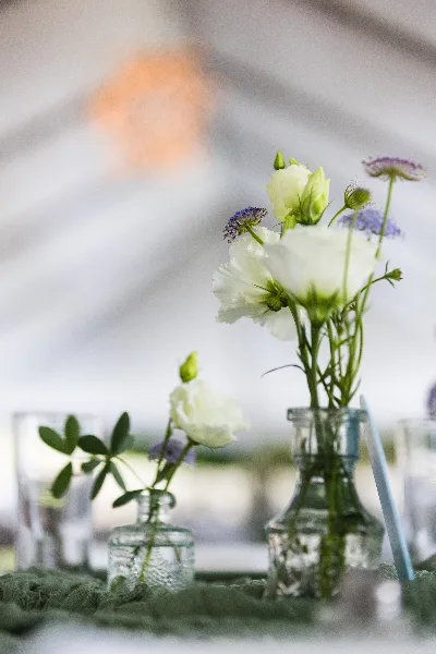 A floral arrangement featuring white lisianthus and purple scabiosa in a clear glass vase on a table.