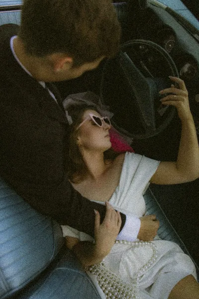 A bride and groom posing intimately in the back seat of a vintage car.