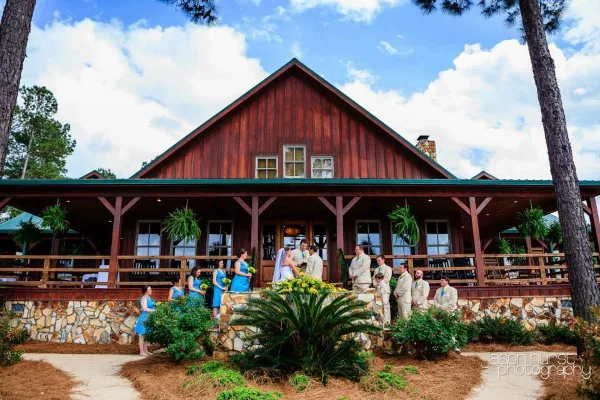 A rustic wooden lodge with a stone foundation and a wedding party posing on the front steps.
