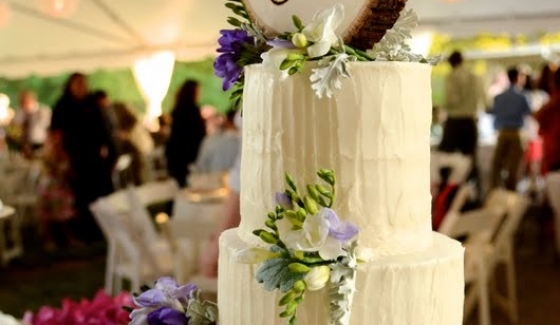 A three-tiered white wedding cake with floral decorations at a reception.