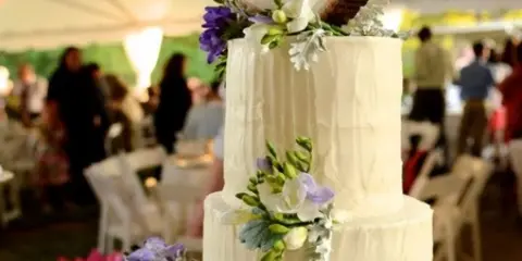 A three-tiered white wedding cake with floral decorations at a reception.