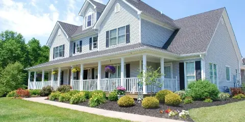 Exterior view of a two-story white house with a porch and landscaped garden.