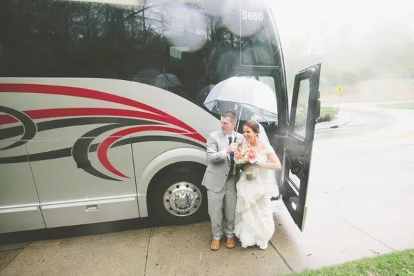 A bride and groom standing in front of a white shuttle bus with red and black graphics.