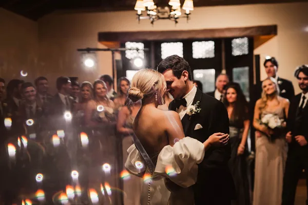 A bride and groom sharing a first dance at a wedding reception, surrounded by guests and wedding party members.