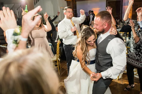 A bride and groom dancing at a wedding reception while guests cheer and raise their hands.