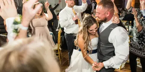 A bride and groom dancing at a wedding reception while guests cheer and raise their hands.