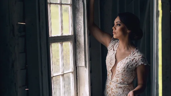 Bride in a lace wedding gown standing by a rustic window in a wedding photography portrait.