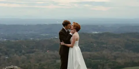 A bride and groom kissing on a rocky overlook with a vast landscape in the background.