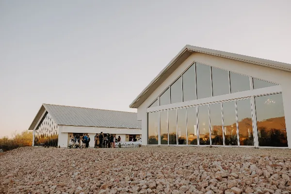 Exterior view of a modern white wedding venue with large glass windows and a gravel foreground.