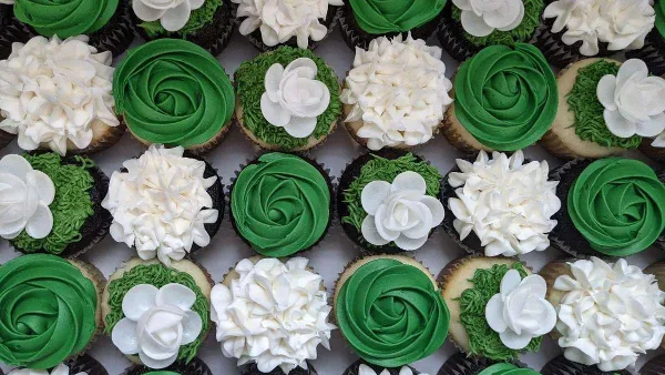 Assortment of cupcakes topped with green and white frosting and white flower decorations.