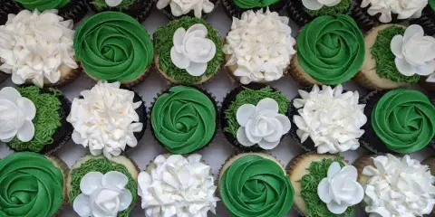 Assortment of cupcakes topped with green and white frosting and white flower decorations.