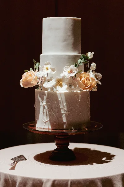 Three-tier ivory buttercream wedding cake with peach roses and white sugar flowers