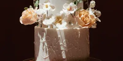Three-tier ivory buttercream wedding cake with peach roses and white sugar flowers