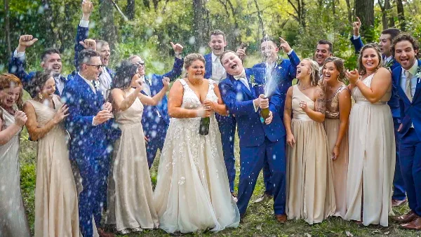 A bride and groom celebrating with their wedding party outdoors, spraying champagne.